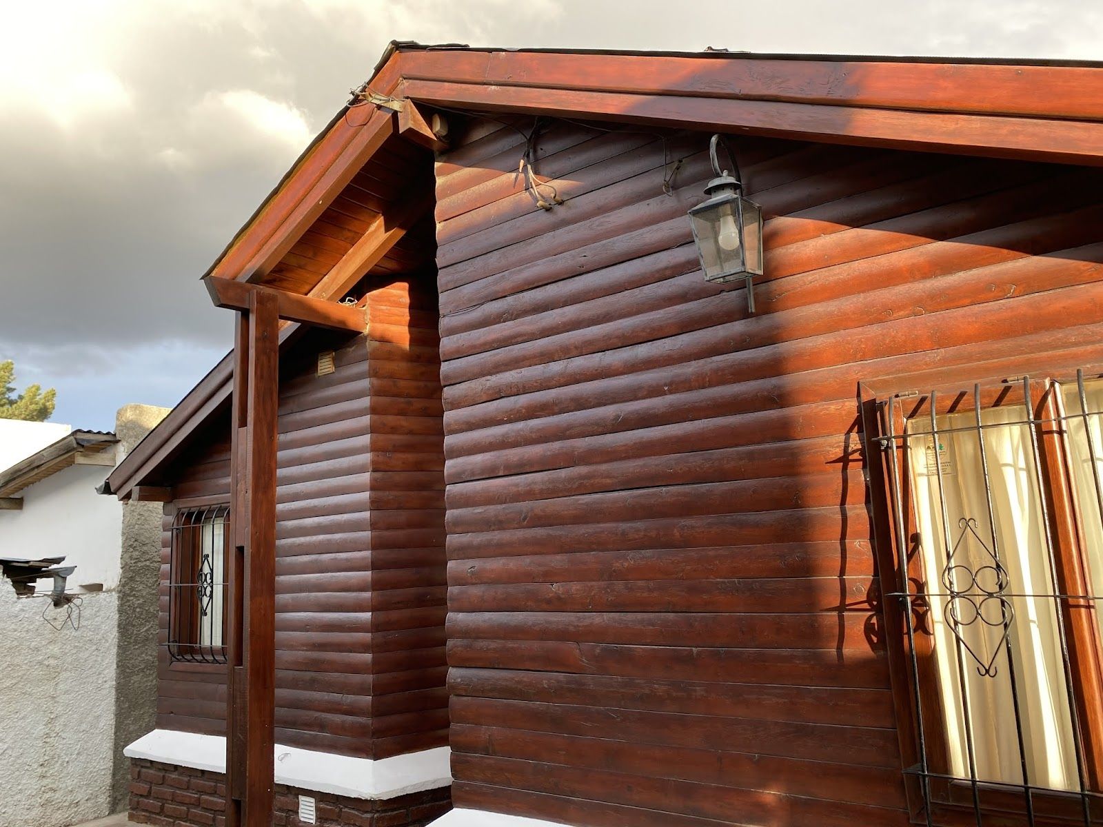 Fachada de madera de una cabaña de Cerro la Zeta con un farol encendido, a la última luz de la tarde