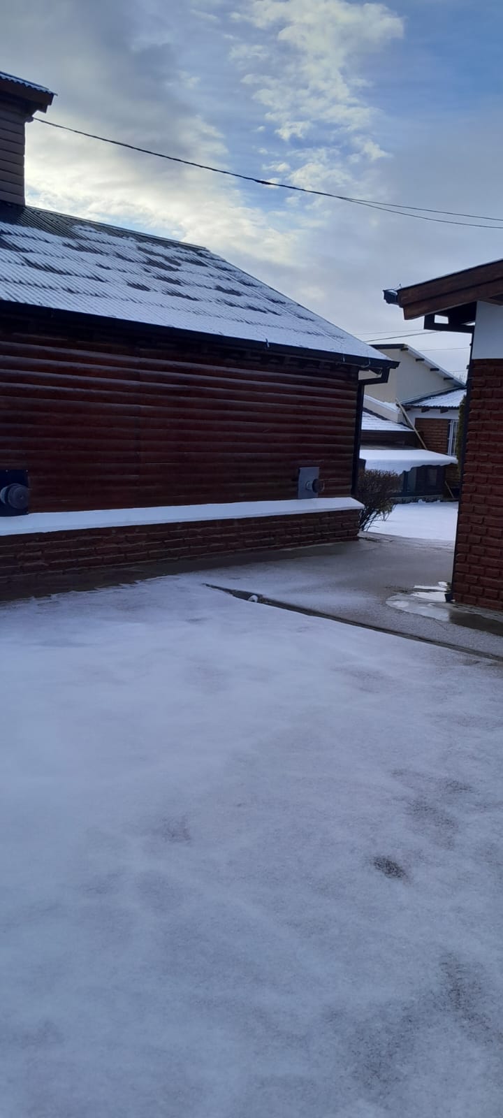 Frente de una cabaña con el techo y el patio cubiertos de nieve, en pleno invierno de Esquel