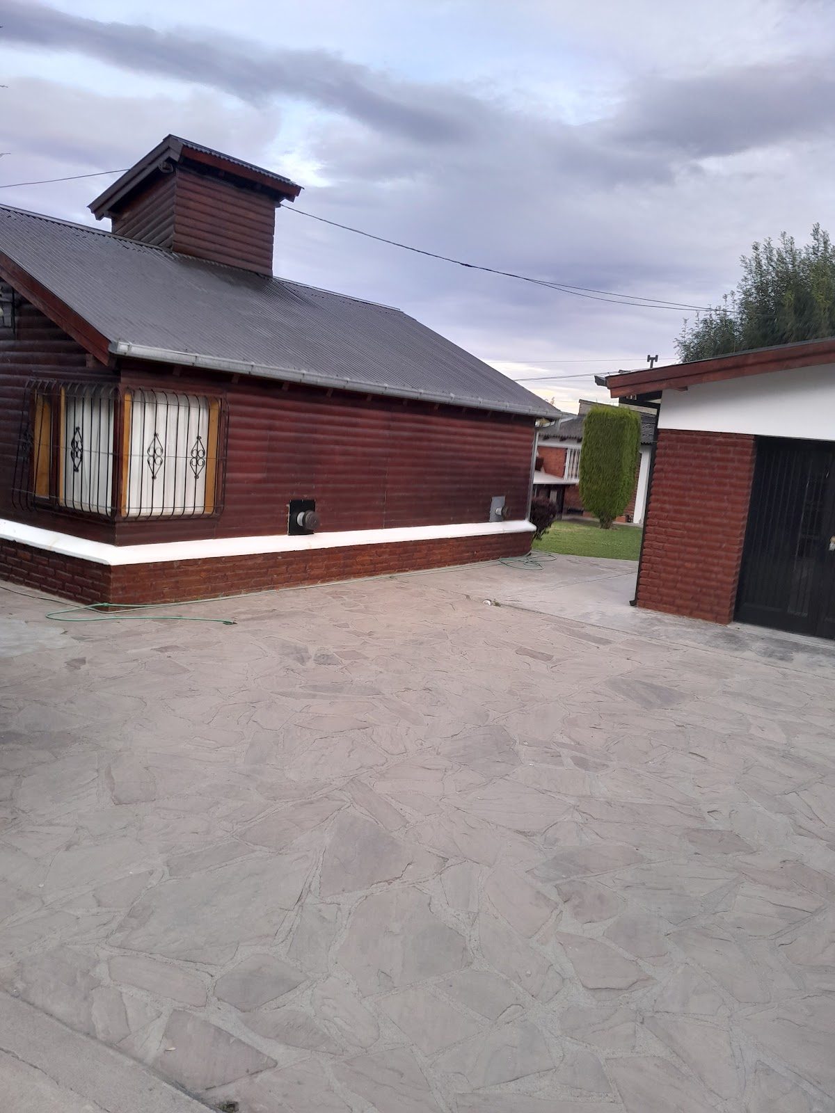 Frente de una cabaña de madera con su cochera, bajo el cielo patagónico