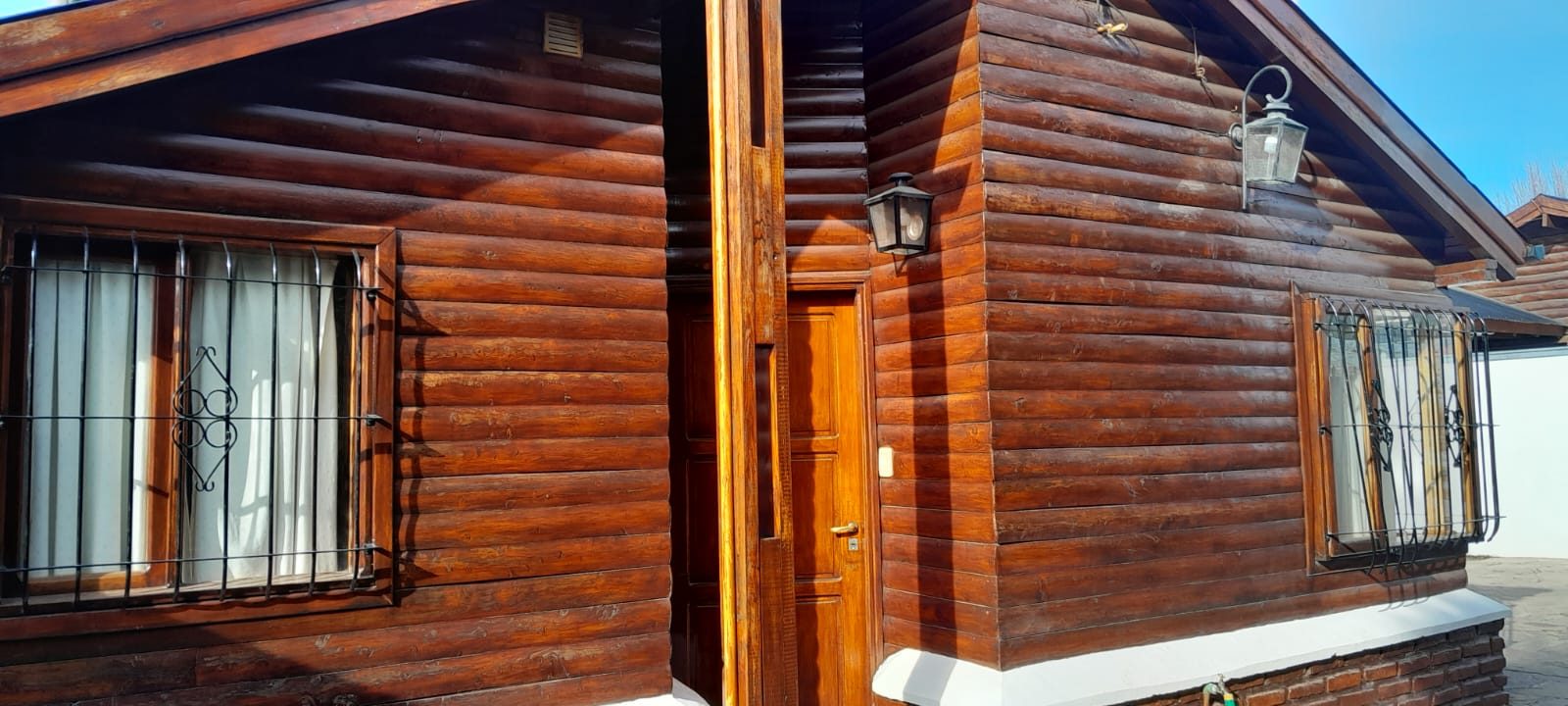 Frente de troncos barnizados de una cabaña, con su puerta de madera y los faroles