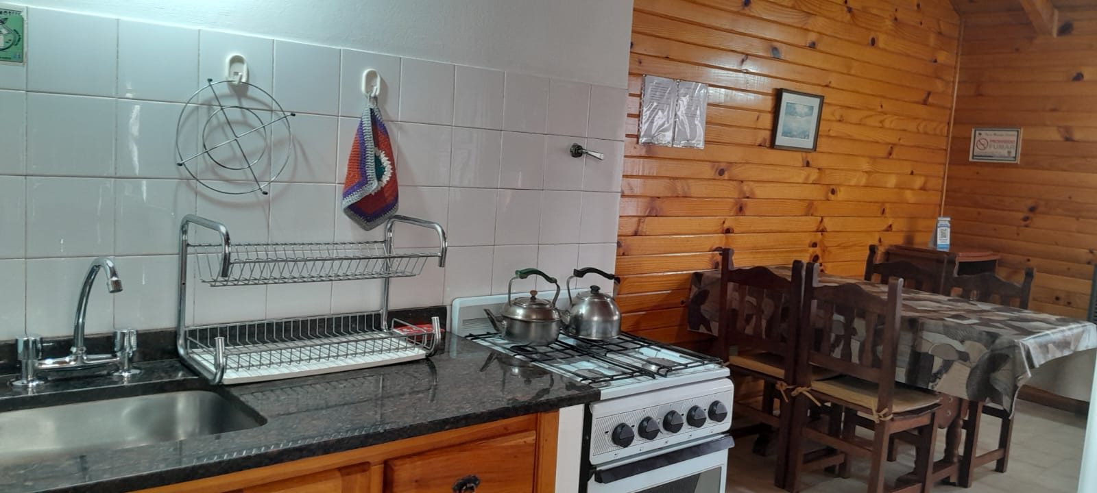 Cocina con mesada de granito, bacha, cocina a gas y las pavas listas, y el comedor de madera al fondo