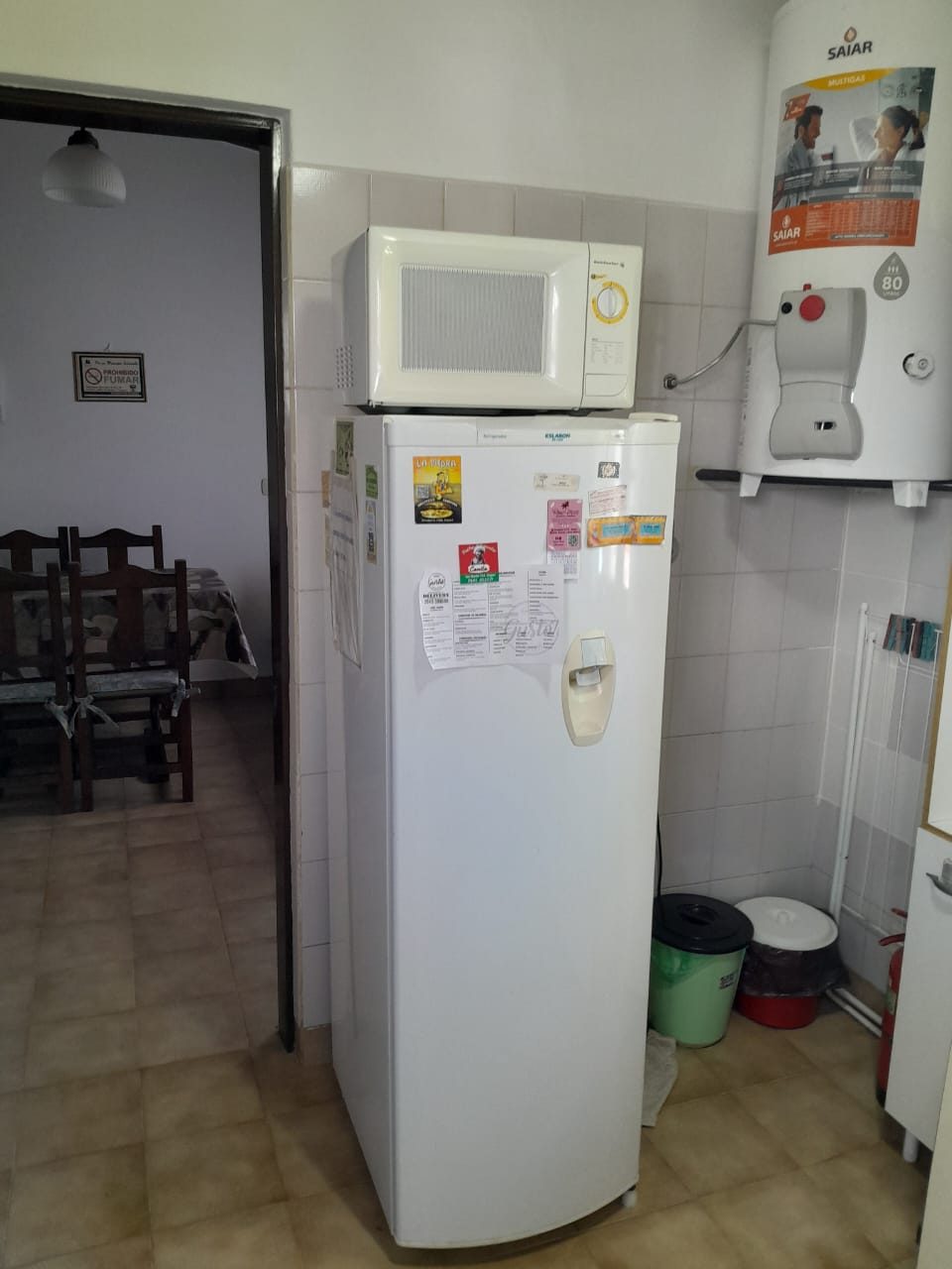 Heladera con freezer y microondas en la cocina, y el comedor asomando al fondo