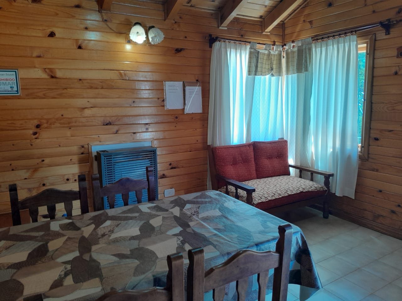 Comedor con la mesa puesta, sillas de madera y el sillón junto a la ventana