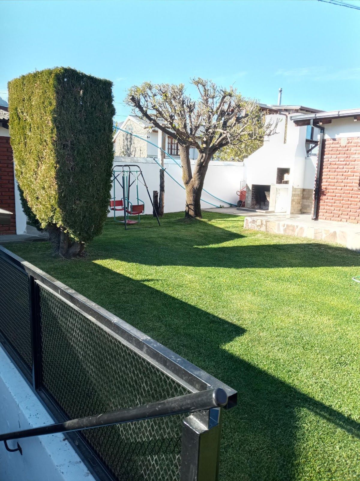Parque verde del complejo con hamaca, árboles y la parrilla al fondo