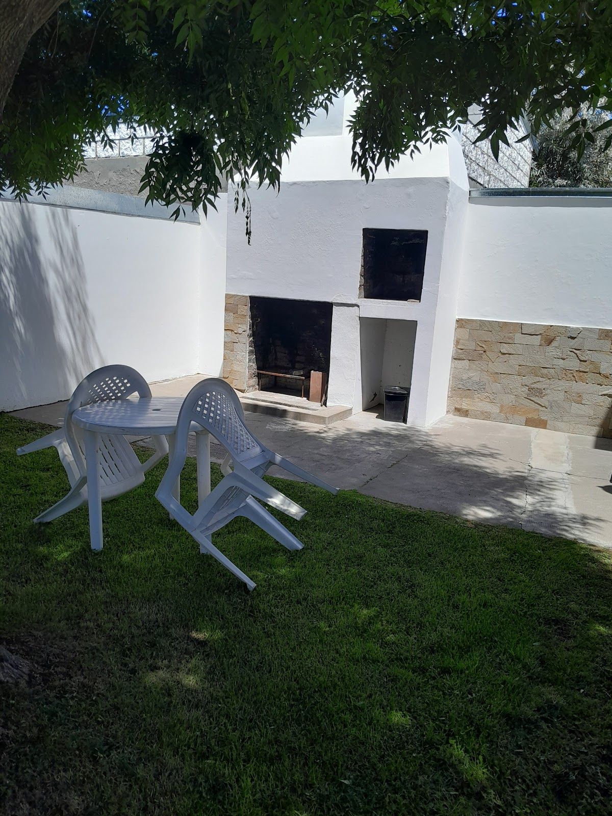 Parrilla de material y mesa a la sombra de un árbol, en el parque
