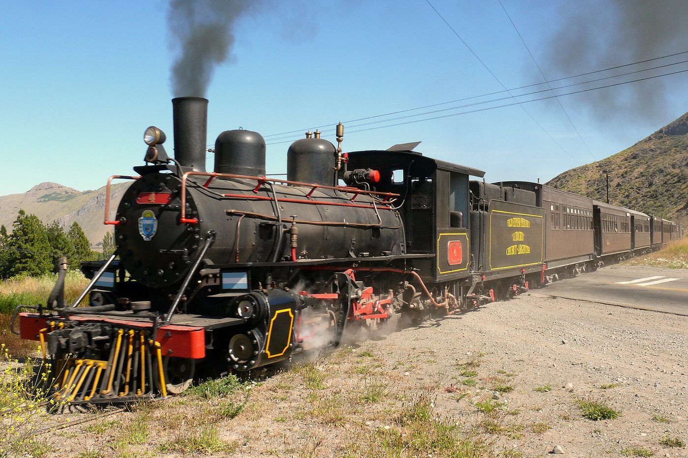 La locomotora a vapor de La Trochita de frente, humeando, con los cerros de Esquel de fondo